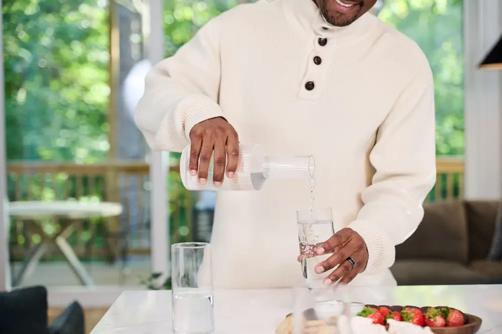 A man pours a class of water from a carafe
