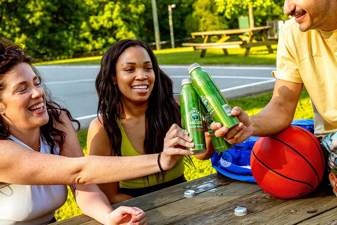 Friends enjoying Mountain Valley Springs aluminum water bottles at a park basketball court