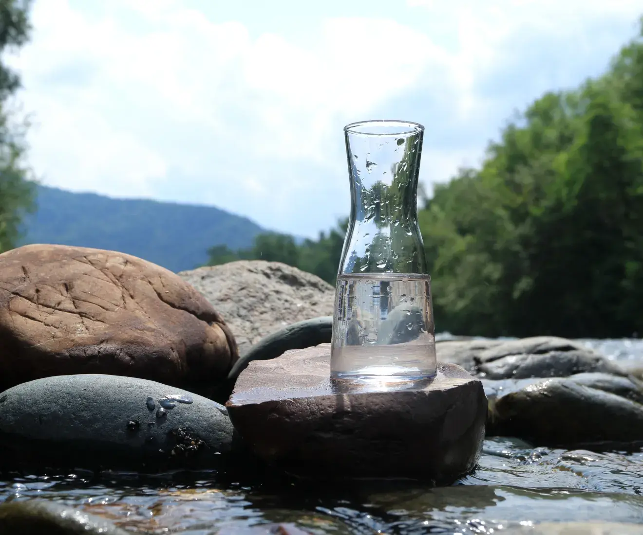 Carafe of water sitting on large stones in a stream