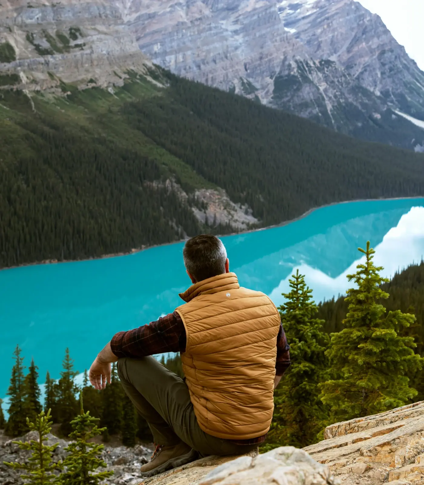 Man sits on a pine mountain ledge overlooking river in ravine