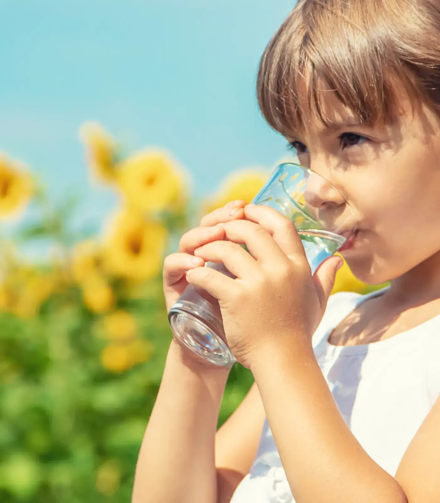 Young girl drinking a glass of whater on a sunny day infront of flowers